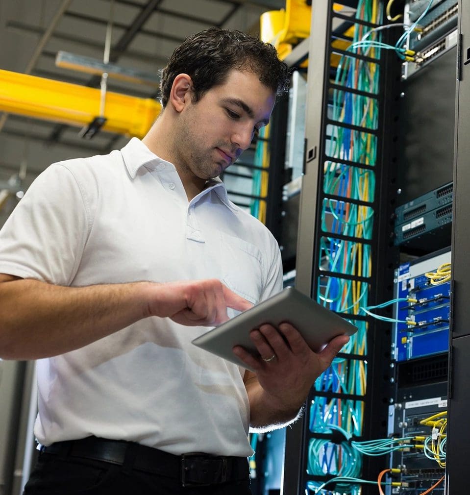 A man in white shirt holding a tablet near rack.