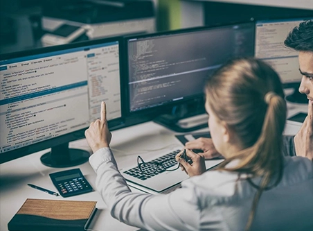 A woman sitting at her desk with two computers.