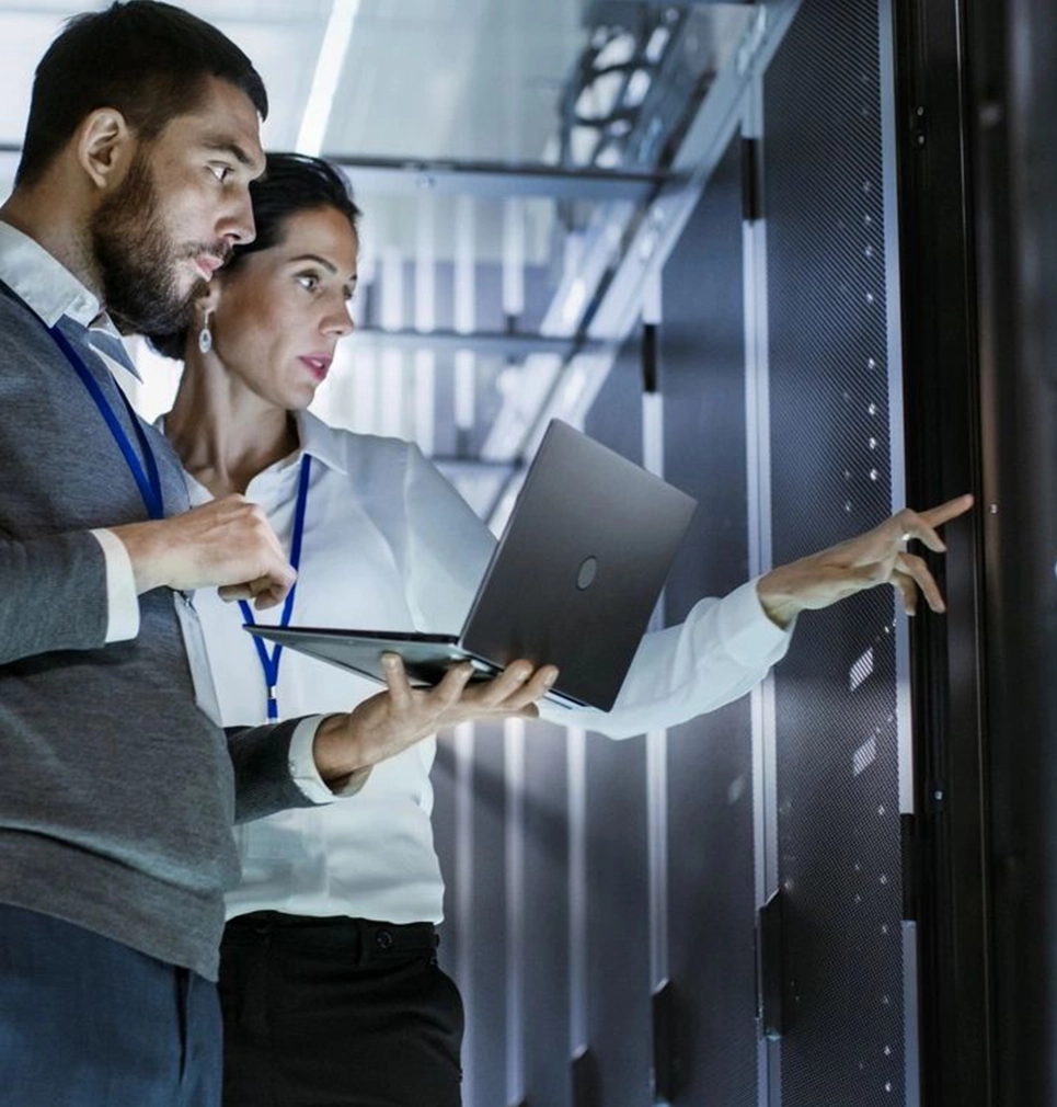 Two people are standing in a room with laptops.